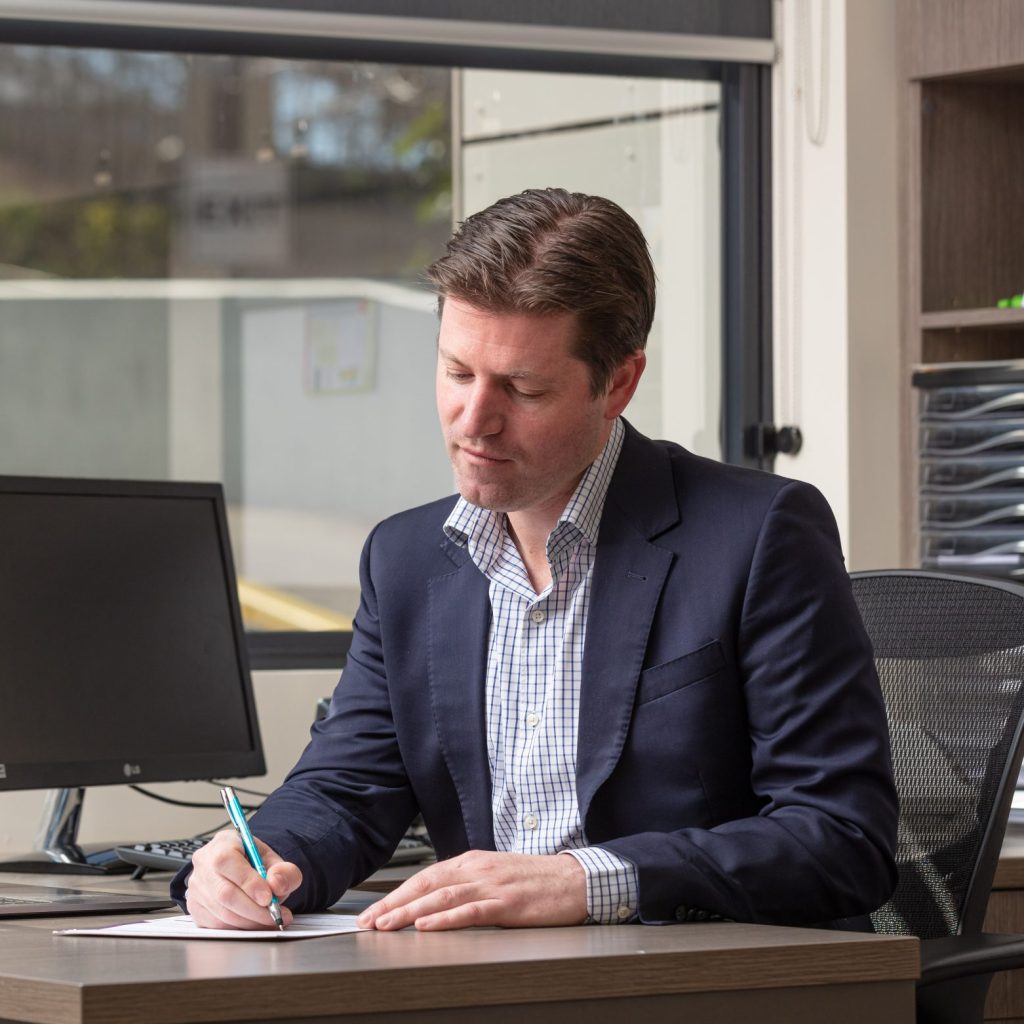 Dr Adam Woodbridge in consulting rooms preparing clinical notes.